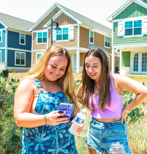 Two young women standing outside using a smart phone