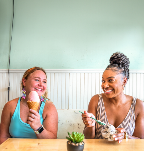 Two young women eating ice cream and smiling at each other