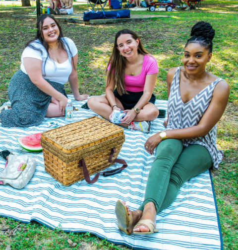 Three young women eating a picnic outside on the grass